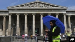 FILE - A worker holding an umbrella guides tourists at the British Museum during a hot weather day in central London, June 12, 2023. The museum reported on Aug. 16, 2023, that items from its collection were found to be missing, stolen or damaged.