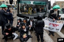 Pengunjuk rasa Yahudi ultra-ortodoks duduk di depan bus sebagai ungkapan protes atas seruan wajib militer untuk memperkuat angkatan bersenjata Israel, di Yerusalem, 18 Maret 2024. (AHMAD GHARABLI/AFP)