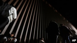 FILE - People line up against a border wall as they wait to apply for asylum after crossing the border from Mexico, July 11, 2023, near Yuma, Arizona.