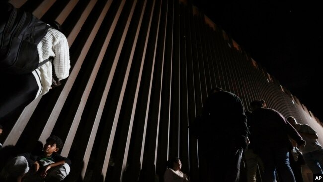 FILE - People line up against a border wall as they wait to apply for asylum after crossing the border from Mexico, July 11, 2023, near Yuma, Arizona.