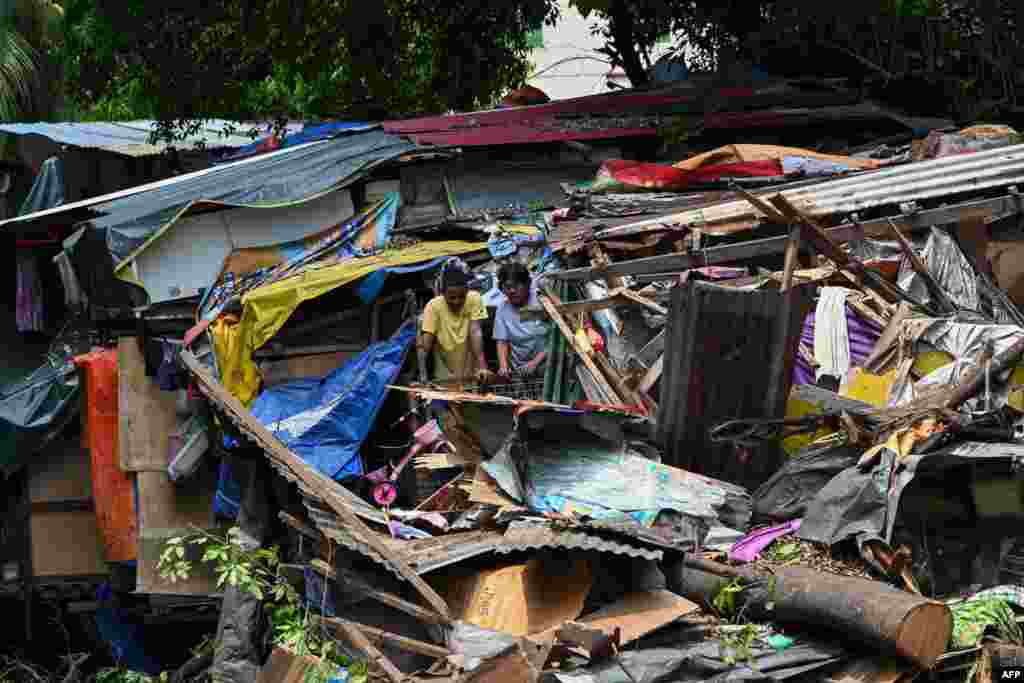 People inspect the damage after a huge tree fell on informal settler homes along a creek in Manila, Philippines.