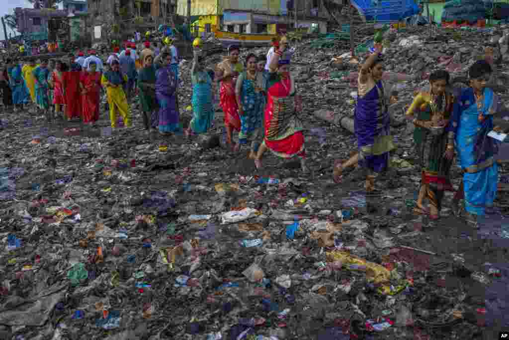 Anggota komunitas nelayan berjalan melalui pantai yang tercemar untuk menawarkan sesaji kelapa ke laut untuk merayakan Narali Purnima, atau festival kelapa, di Mumbai, India. (AP)&nbsp;