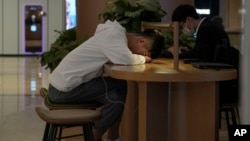 A man takes a nap next to another who browses on a computer at a mall cafe in Beijing on May 24, 2023. China’s consumer and factory activity has weakened, and unemployment among city youths has hit record levels.