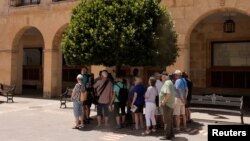FILE - A group of tourists hide from the strong midday sun under the shadow of a tree, as they listen to their guide during the first heat alert of the year, on a hot spring day, in a street in Ronda, Spain, May 30, 2024.