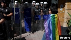 FILE - An activist stands near riot police who prevent activists from marching in a pride parade, which was banned by local authorities, in central Istanbul, June 26, 2022.
