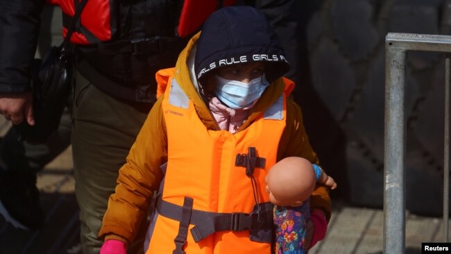 Një fëmijë emigrant mban një kukull me vete pas zbarkimit në tokën angleze
