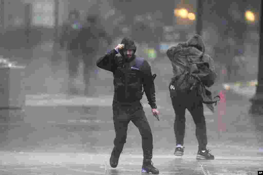 Pedestrians struggle to walk through wind and rain as they cross a street in Boston, Massachusetts.