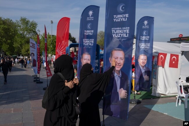 FILE - A woman gestures in front of a banner with an image of Turkish President and People's Alliance's presidential candidate Recep Tayyip Erdogan, in Istanbul, Turkey, Monday, May 8, 2023. Turkey is heading toward presidential and parliamentary elections on Sunday May 14, 2023. (AP Photo/Khalil Hamra, File)