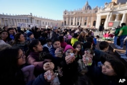 Children hold up statues of baby Jesus as they wait for Pope Francis' Angelus noon prayer he celebrates from the window of his studio overlooking St.Peter's Square, at the Vatican, Dec. 17, 2023.