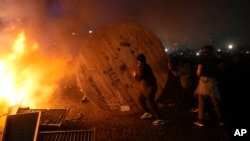 FILE: Demonstrators rolls a wooden cable spool to a burning barricade during a protest in Paris, Friday, March 17, 2023. Many French citizens are enraged at President Macron for pushing through a two-year hike in the full retirement age. 