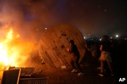 Demonstrators rolls a wooden cable spool to a burning barricade during a protest in Paris, Friday, March 17, 2023.