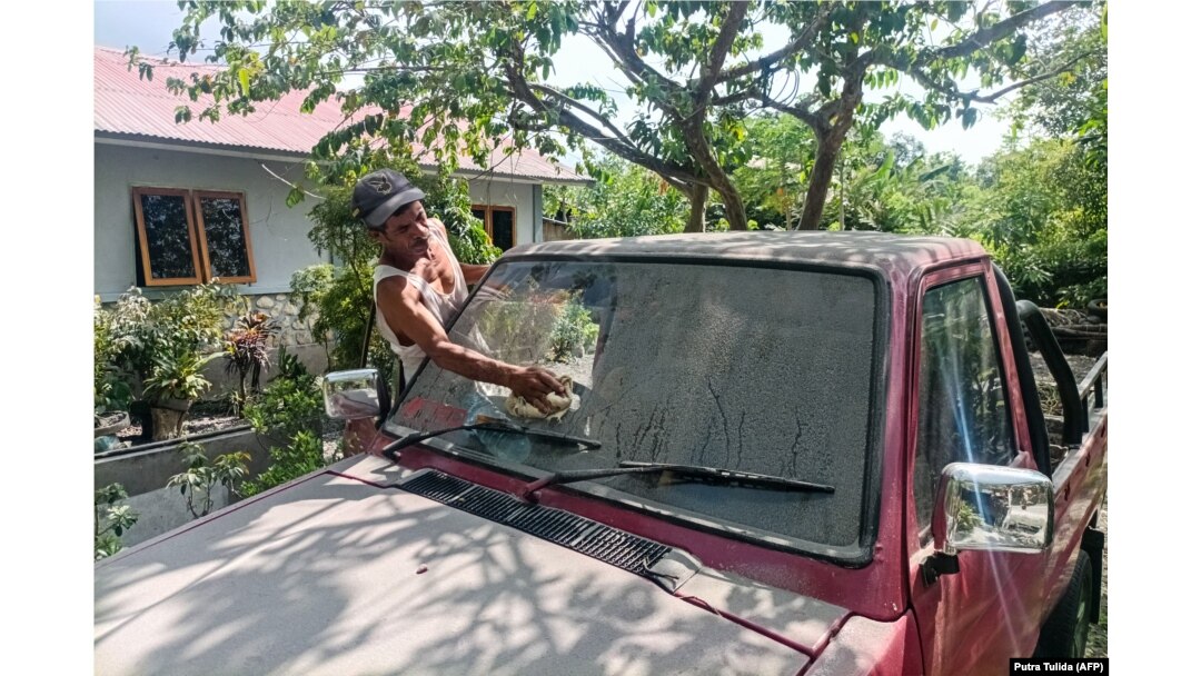 Seorang pria membersihkan abu vulkanik di kaca depan mobilnya usai Gunung Lewotobi Laki-Laki meletus di Klatanlo, Nusa Tenggara Timur pada 23 Desember 2023. (Foto: AFP/Putra Tulida) 