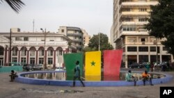 People rest next to a fountain adorned with the Senegalese flag at Place de l'Indépendance, March 20, 2024, ahead of the upcoming presidential elections in Dakar, Senegal. 