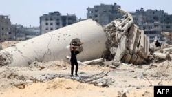 A Palestinian child transporting pieces of wood walks past a building destroyed by Israeli bombardment in Gaza City on May 3, 2024.