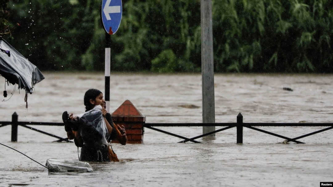 A woman carrying her belongings wades through a flooded road along the bank of overflowing Bagmati River following heavy rains in Kathmandu, Nepal, July 6, 2024. 