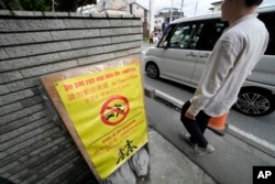 A notice for tourists across the use road from the Lawson convenience store, where a popular photo spot framing a picturesque view of Mount Fuji in the background Tuesday, April 30, 2024, at Fujikawaguchiko in, central Japan. (AP Photo/Eugene Hoshiko)