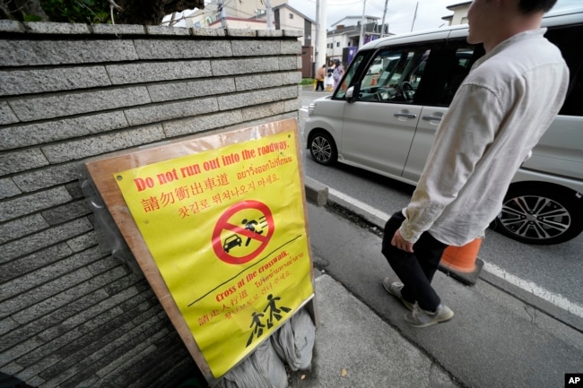 A notice for tourists across the use road from the Lawson convenience store, where a popular photo spot framing a picturesque view of Mount Fuji in the background Tuesday, April 30, 2024, at Fujikawaguchiko in, central Japan. (AP Photo/Eugene Hoshiko)