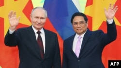 In this pool photograph distributed by the Russian state agency Sputnik, Russia's President Vladimir Putin (L) and Vietnam's Prime Minister Pham Minh Chinh (R) wave as they pose for photos at the Government Office in Hanoi, on June 20, 2024.