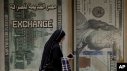 FILE - An Egyptian woman walks past an exchange office in Cairo, Egypt, March 6, 2024. 