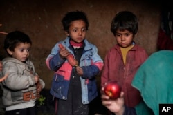 Three internally displaced children look with surprise at an apple that their mother brought home after begging, in a camp on the outskirts of Kabul, Afghanistan, Thursday, Feb 2, 2023. (AP Photo/Ebrahim Noroozi)