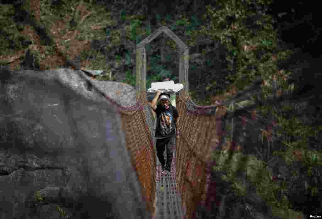 Cornelius Mawa, 28, a porter, carries Voter Verifiable Paper Audit Trail and Electronic Voting Machines as he crosses a suspension bridge to reach a distant polling station in Shillong in the northeastern state of Meghalaya, India, April 17, 2024.