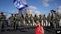 A demonstrator waves the Israeli flag seated on a highway while flanked by paramilitary border police during a protest against plans by Prime Minister Benjamin Netanyahu's government to overhaul the judicial system, in Tel Aviv, Israel, March 9, 2023.