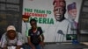 FILE - Passengers sit at a bus station beside a billboard of President Bola Tinubu and Vice President Kashim Shettima, while waiting at a bus station in Lagos, June 1, 2023. Nigerian consumers are lamenting the ripple effect of the removal of the fuel subsidy.