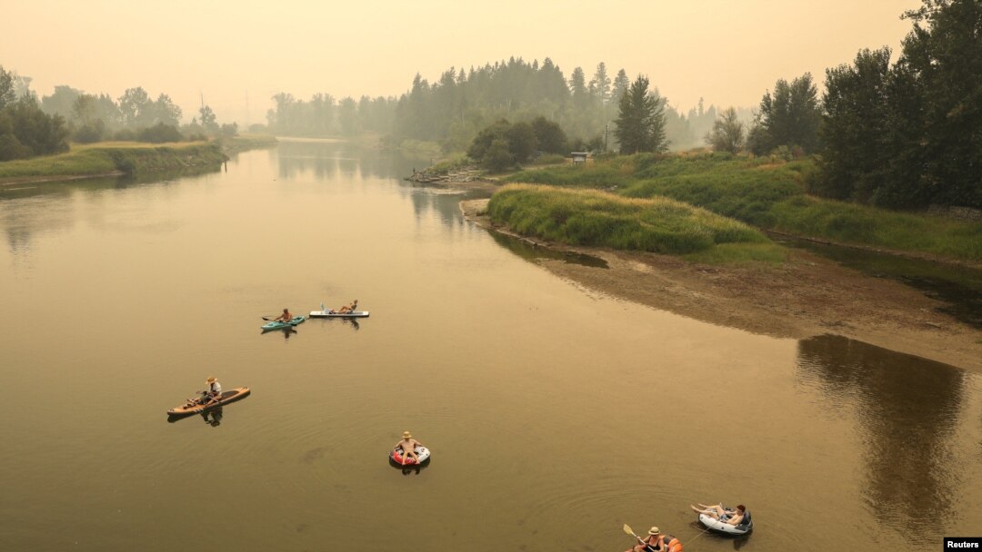 Sejumlah orang tampak berada di sungai Shuswap di saat asap dari kebakaran hutan menyelimuti lembah di wilayah Enderby, British Columbia, Kanada, pada 19 Agustus 2023. (Foto: Reuters/Chris Helgren)