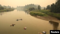 Sejumlah orang tampak berada di sungai Shuswap di saat asap dari kebakaran hutan menyelimuti lembah di wilayah Enderby, British Columbia, Kanada, pada 19 Agustus 2023. (Foto: Reuters/Chris Helgren)