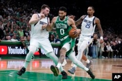 El alero de los Boston Celtics, Jayson Tatum (0), conduce el balón mientras el escolta de los Dallas Mavericks, Luka Doncic, y el alero P.J. Washington (25) defienden durante el partido de las finales de baloncesto de la NBA, el lunes 17 de junio de 2024, en Boston.