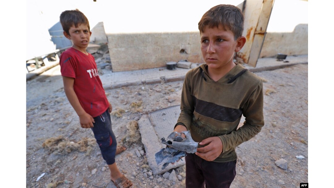 A boy holds a piece of metal as he stands with another youth after Russian airstrikes hit an abandoned water pumping station in Syria's rebel-held northwest, Aug. 23, 2023.