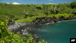 People spend time on the black sand beach at Waianapanapa State Park in Hana, Hawaii, on Sept. 24, 2014. (AP Photo/Marco Garcia, File)