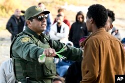 U.S. Border Patrol agents hand out bracelets as they they process asylum seekers waiting between the double fence along the U.S.-Mexico border near Tijuana, Mexico, May 8, 2023, in San Diego.