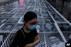 FILE - A pedestrian passes smiling portraits on display as part of the installation titled 'Inside Out: Harbour and the City' created by French artist JR in Hong Kong, April 26, 2023.