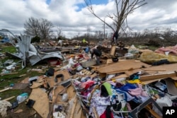 People walk through damage from a late-night tornado in Sullivan, Ind., April 1, 2023. (AP Photo/Doug McSchooler, File)