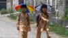 Anak-anak sekolah memakai topi payung, berjalan pulang ke rumah di sepanjang jalan di kota Peshawar, Pakistan. (AFP)