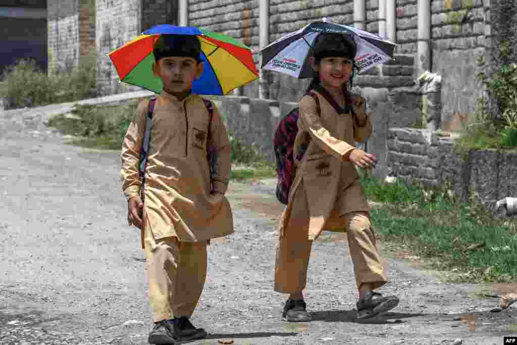 School children wearing umbrella hats, make their way to home along a street in Peshawar, Pakistan.