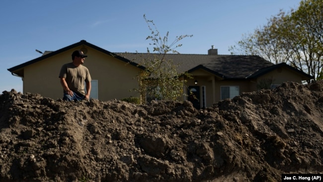 Earl Gomes, 33, stands for a photo outside his home with a berm he built to protect the property from possible flooding of the Kings River in the Island District of Lemoore, Calif., Thursday, April 20, 2023. (AP Photo/Jae C. Hong)