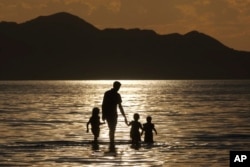 A family walks in the water during sunset at the Great Salt Lake on June 13, 2024, near Salt Lake City.
