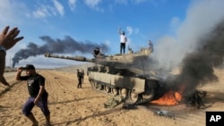 Palestinians celebrate by a destroyed Israeli tank at the Gaza Strip fence, Oct. 7, 2023.