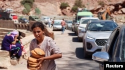 A girl carries bread received from a volunteer as people in vehicles wait for the road to be cleared from debris in the aftermath of a deadly earthquake near the village of Tallat n'Yakoub, Morocco, Sept. 12, 2023
