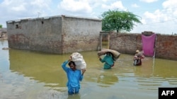 A family displaced by flood, carry their belongings as they wade through floodwaters after heavy monsoon rains at Sohbatpur in Jaffarabad district, Balochistan province, Pakistan, Aug. 19, 2024. 