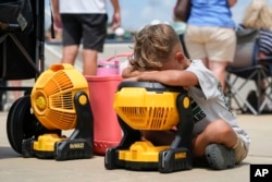 FILE - Braxton Hicks, 7, of Livingston, Texas, holds his face to a portable fan to cool off during a baseball tournament in Ruston, La., Aug. 9, 2023. (AP Photo/Gerald Herbert)