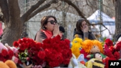 People react as they stand in front of toys and flowers displayed outside a multi-story building heavily damaged in Odesa on March 3, 2024.