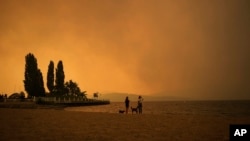 ARCHIVO - El humo del incendio de McDougall Creek llena el aire mientras dos personas miran el paisaje en el lago Okanagan desde la playa Tugboat, en Kelowna, Columbia Británica, el 18 de agosto de 2023.