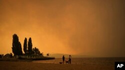 Smoke from the McDougall Creek wildfire fills the air and nearly blocks out the sun as people take in the view of Okanagan Lake from Tugboat Beach, in Kelowna, British Columbia, Canada, Aug. 18, 2023.