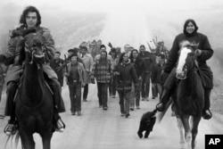 FILE - Assistant U.S. Attorney General Harlington Wood, third row center without hat, is escorted into the village of Wounded Knee , South Dakota, by members of the American Indian Movement, March 13, 1973.