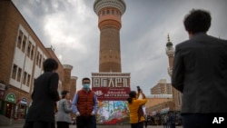 FILE - Tourists take photos near a tower at the International Grand Bazaar in Urumqi in western China's Xinjiang Uyghur Autonomous Region, as seen during a government-organized trip for foreign journalists on April 21, 2021.
