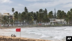 Turis duduk di pantai La Pared saat Badai Tropis Ernesto melewati Luquillo, Puerto Riko, Selasa, 13 Agustus 2024. (Alejandro Granadillo/AP)