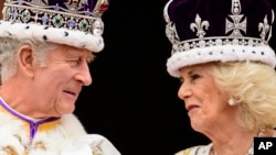 Raja Charles III dan Ratu Camilla saling menatap satu sama lain di saat mereka berada di balkon Istana Buckhingham, London, selepas acara penobatan pada 6 Mei 2023. (Foto: Leon Neal/Pool Photo via AP)